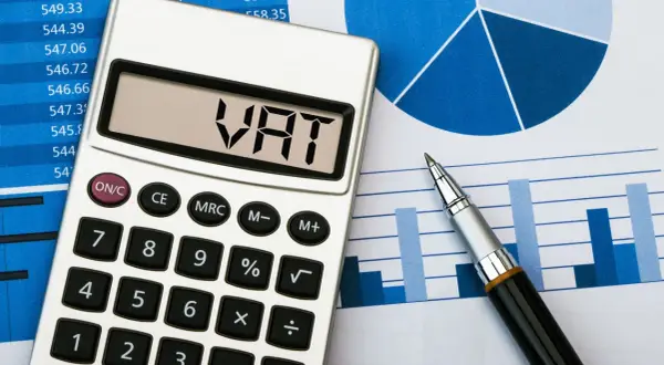 Kalkulator z napisem VAT na wyświetlaczu leży obok wykresów i długopisu. Przygotowanie do rozliczenia JPK VAT.