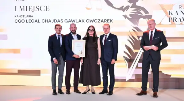 Cztery osoby w garniturach stoją na scenie, odbierając nagrodę.