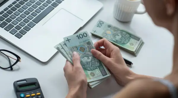 Kobieta liczy banknoty 100 zł, obok laptop, kalkulator i okulary. Czy to kwota wolna od zajęcia?