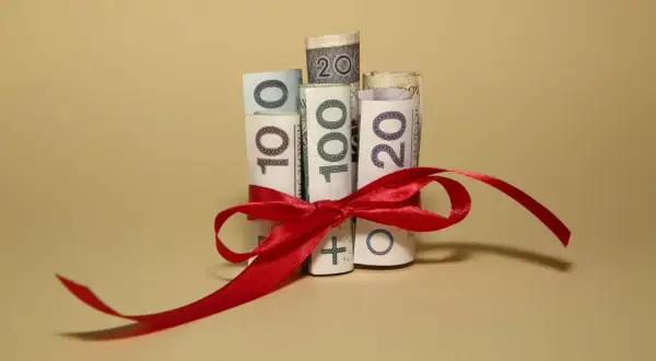Zwijane banknoty 10, 20 i 100 zł związane czerwoną wstążką. Pomyśl o tym jak o prezencie, ale pamiętaj o podatku od spadków i darowizn.