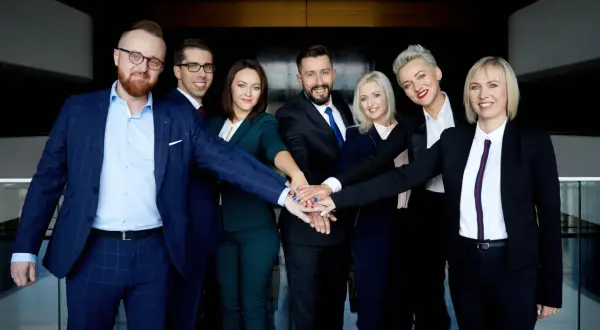 Grupa prawników w garniturach z rękami złożonymi na środku.