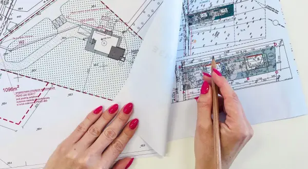 Ręka z różowymi paznokciami wskazuje ołówek na mapie do celów projektowych, gdzie widoczne są plany budowy przyłącza wodociągowego.