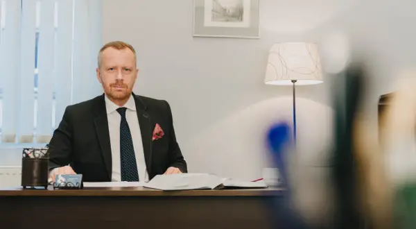Mężczyzna w garniturze siedzi przy biurku, przed nim otwarta księga.