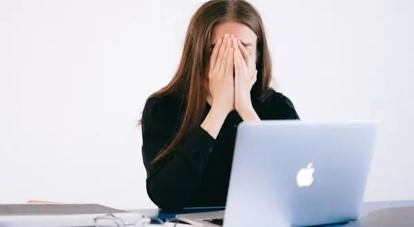 Kobieta z dłońmi na twarzy, przygnębiona przez zniesławienie w internecie.