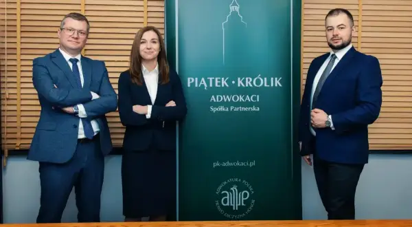Trzy osoby w garniturach stoją przed zielonym banerem kancelarii.