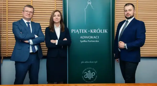 Trzy osoby w garniturach stoją przed zielonym banerem kancelarii "Piątek • Królik Adwokaci".