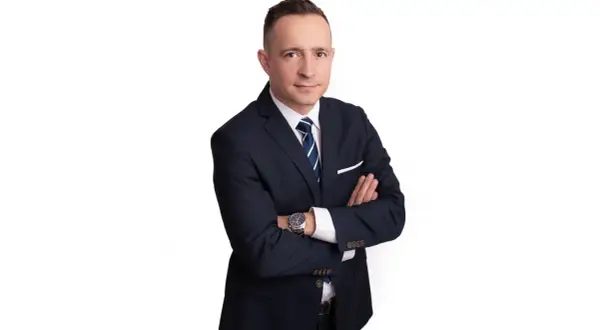 Mężczyzna w garniturze z rękami skrzyżowanymi na piersi, na białym tle.