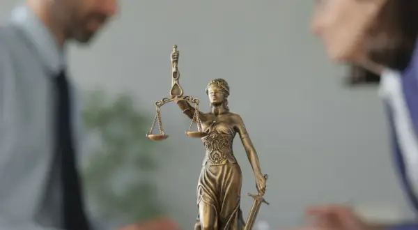 Figurka Temidy z wagą i mieczem na tle niewyraźnych postaci prawników.
