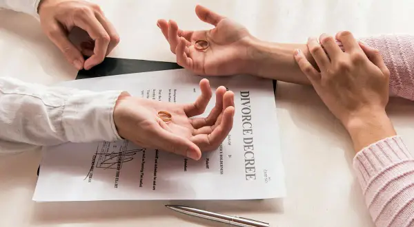 Dwie dłonie trzymają obrączki, leżące na dokumencie "DIVORCE DECREE". Symboliczny koniec małżeństwa, czas na rozwód.