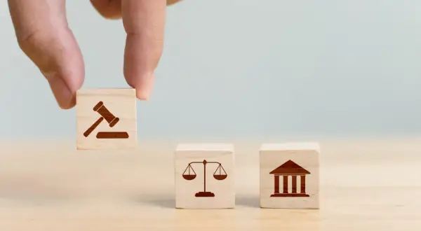 Dłoń układa kostki z symbolami prawa: młotek sędziowski, waga sprawiedliwości i budynek sądu, symbolizujące jurysdykcję.
