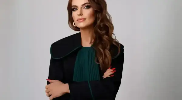 Kobieta w todze prawniczej, z rękami skrzyżowanymi na piersi, na jasnym tle.
