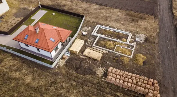 Budowa domu w zabudowie zagrodowej: fundamenty, drewno i cegły czekają na użycie.