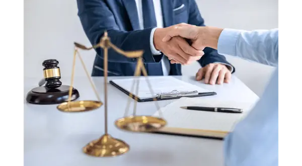 Dwóch prawników ściska sobie dłonie przy biurku, na którym leży młotek sędziowski i waga sprawiedliwości. Sprawa 157 kk zakończona sukcesem.