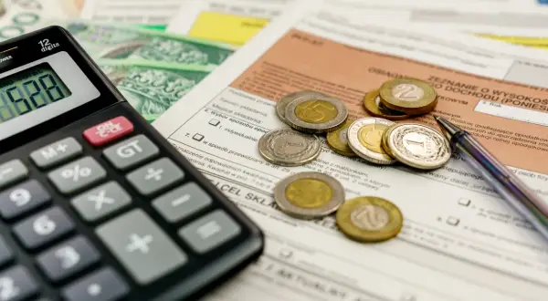 Kalkulator, monety i dokumenty podatkowe leżą na stole, czekając na rozliczenie. Kiedy zwrot podatku jest blisko, liczenie staje się prostsze.