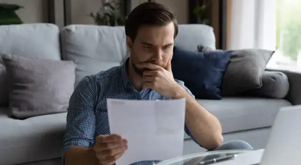 Mężczyzna zamyślony czyta dokumenty przy laptopie.