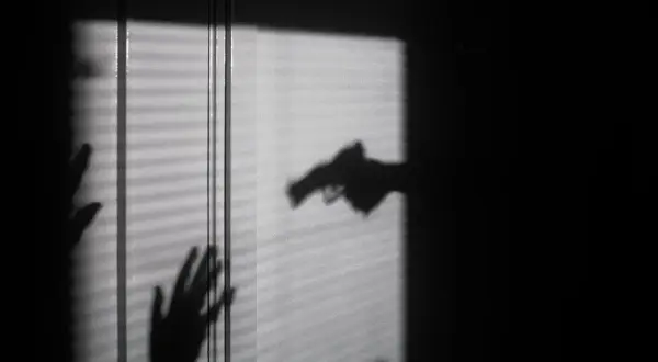 Cień dłoni z pistoletem grozi dwóm dłoniom, które próbują się zasłonić. To scena jak z filmu o świadku koronnym.