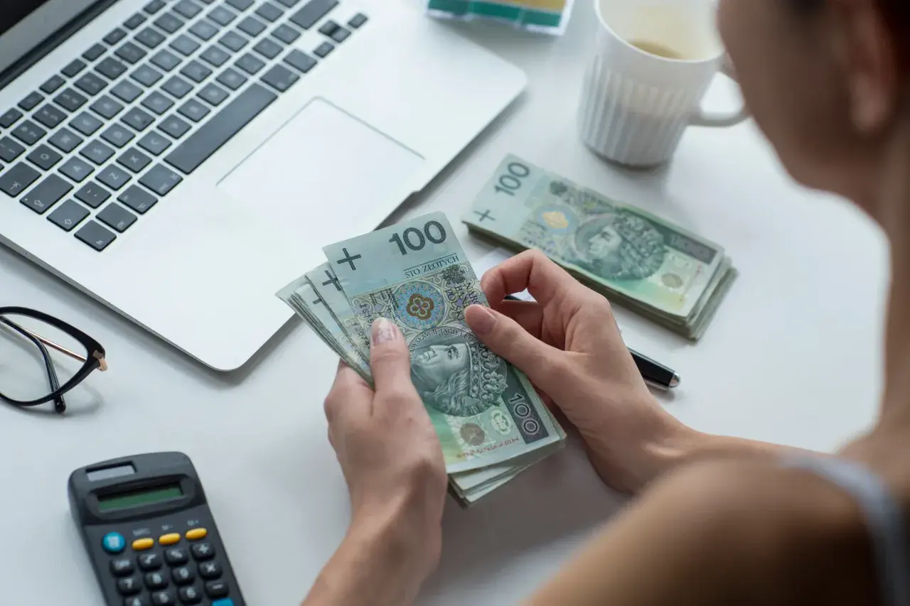 Kobieta liczy banknoty 100 zł, obok laptop, kalkulator i okulary. Czy to kwota wolna od zajęcia?