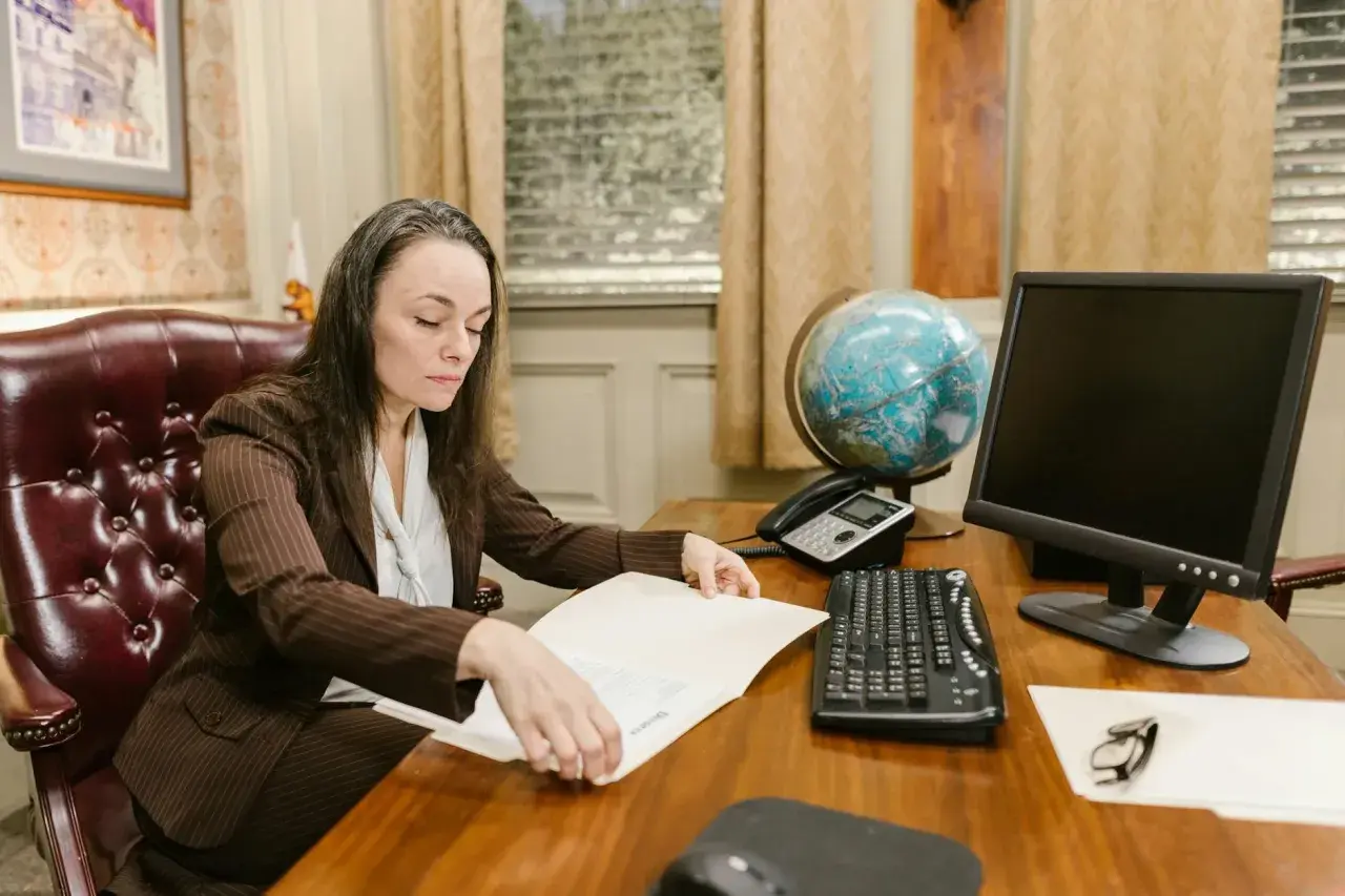 Kobieta w garniturze przegląda dokumenty, przygotowując się do wejścia w życie nowego prawa. Na biurku globus, telefon i komputer.