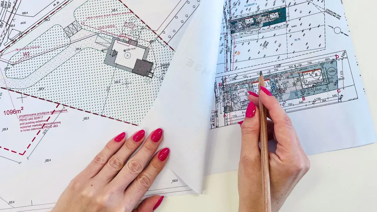 Ręka z różowymi paznokciami wskazuje ołówek na mapie do celów projektowych, gdzie widoczne są plany budowy przyłącza wodociągowego.