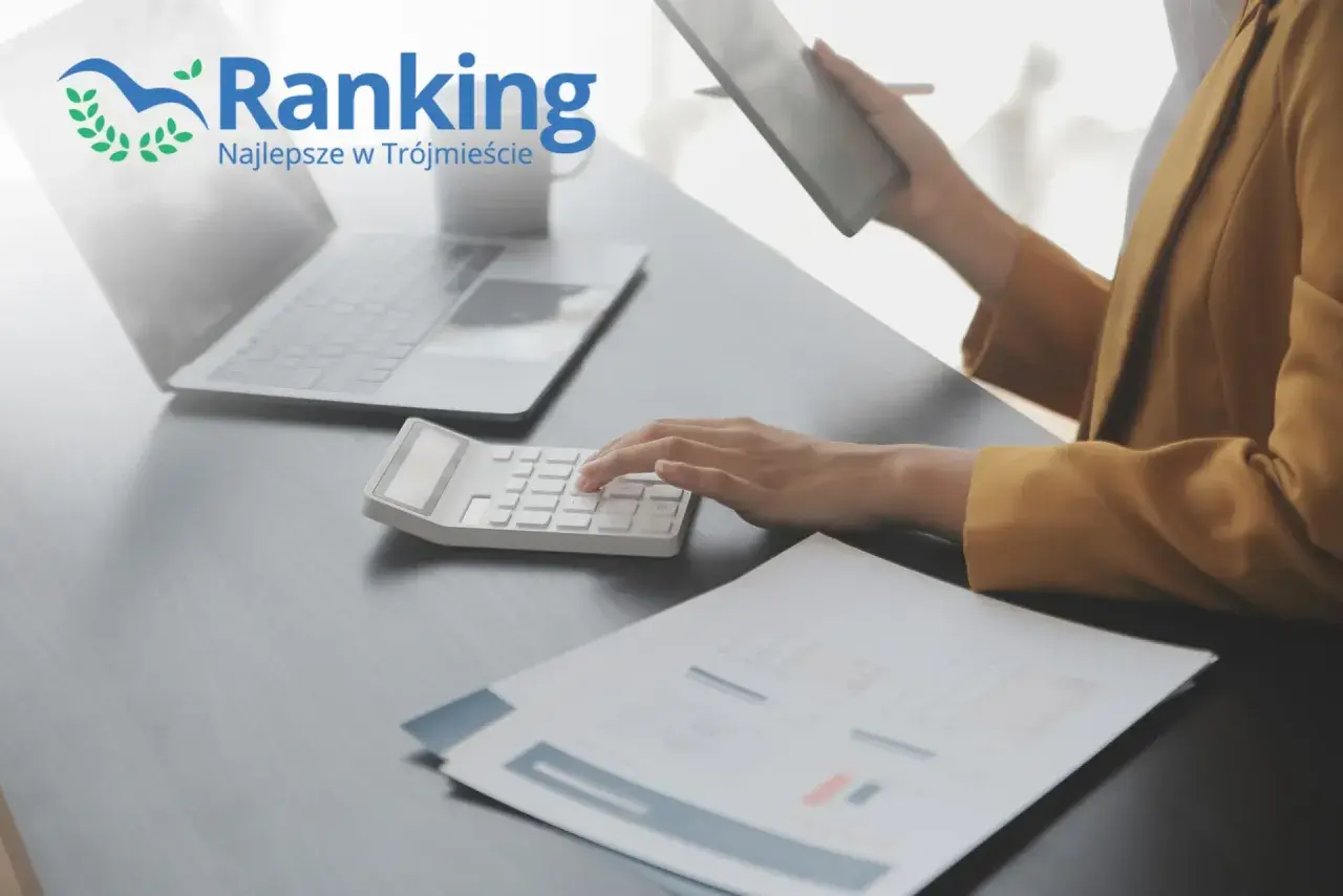 Ręce na kalkulatorze, laptop i tablet na biurku, logo "Ranking Najlepsze w Trójmieście".