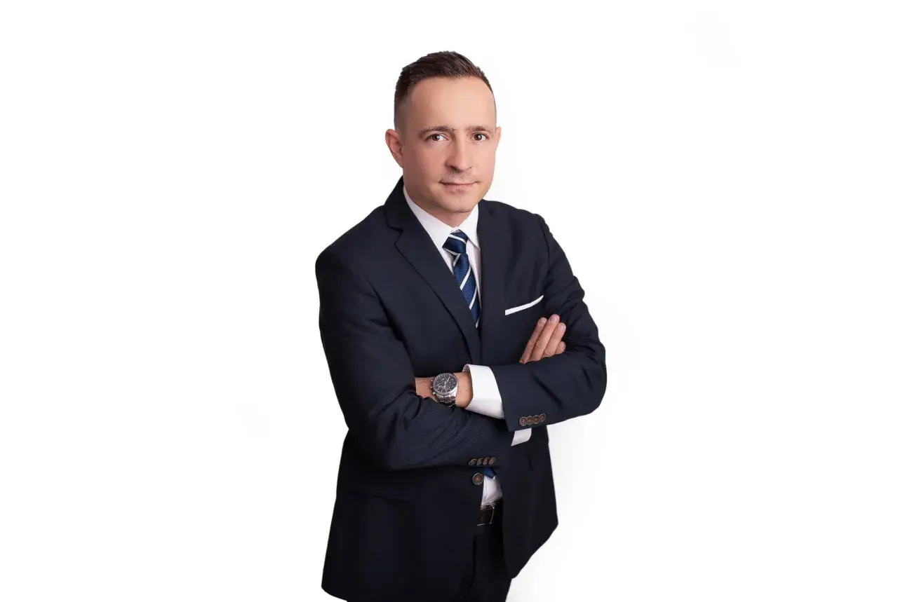 Mężczyzna w garniturze z rękami skrzyżowanymi na piersi, na białym tle.