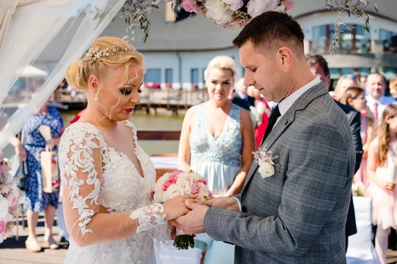 Para młoda podczas ceremonii ślubnej. Panna młoda w koronkowej sukni, pan młody w garniturze. Pytanie o to, odpis aktu małżeństwa ile ważny, nie ma związku z tą sceną.
