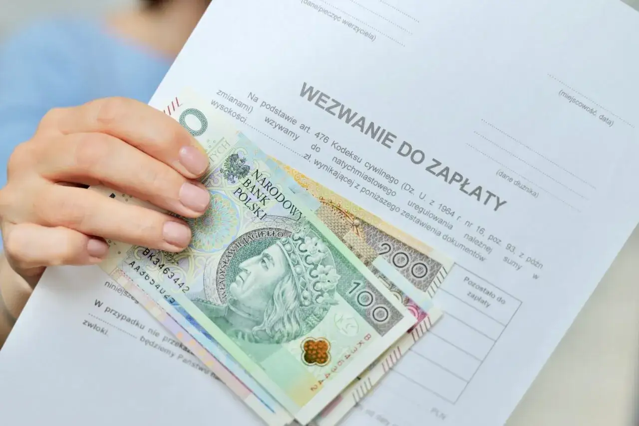 Dłoń trzyma polskie banknoty na dokumencie 