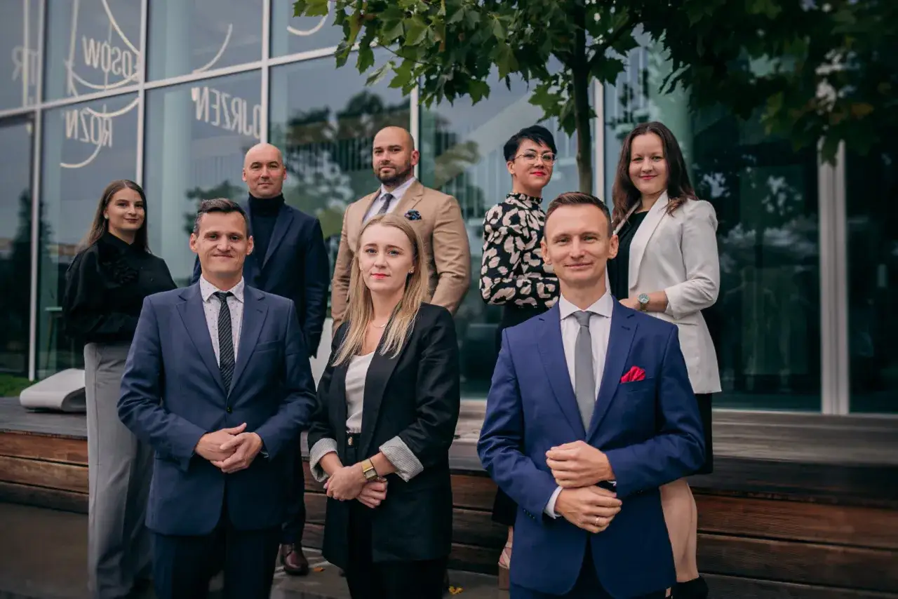 Grupa prawników w eleganckich strojach przed nowoczesnym budynkiem.