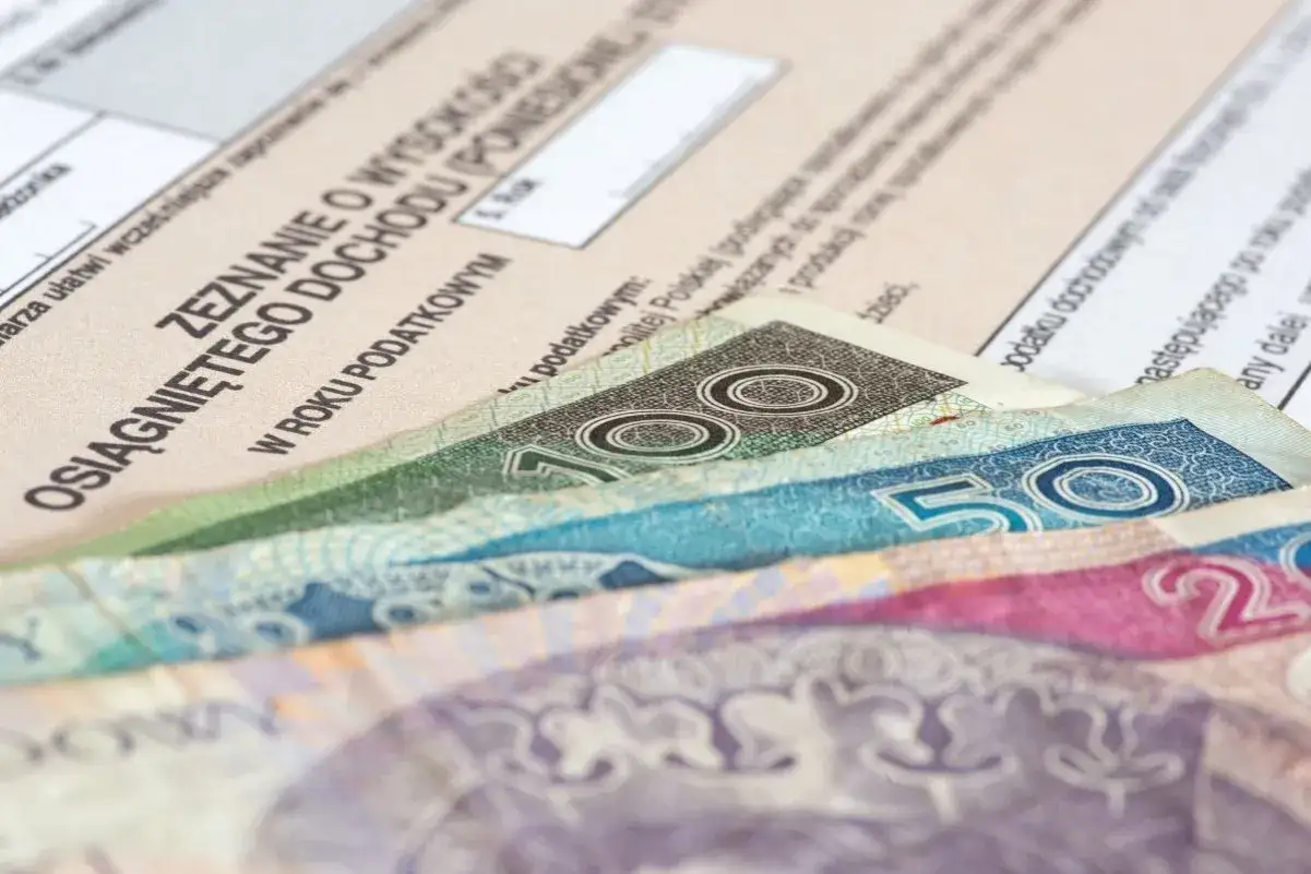 Zeznanie o dochodach i polskie banknoty 100, 50 zł. Karta podatkowa w tle.