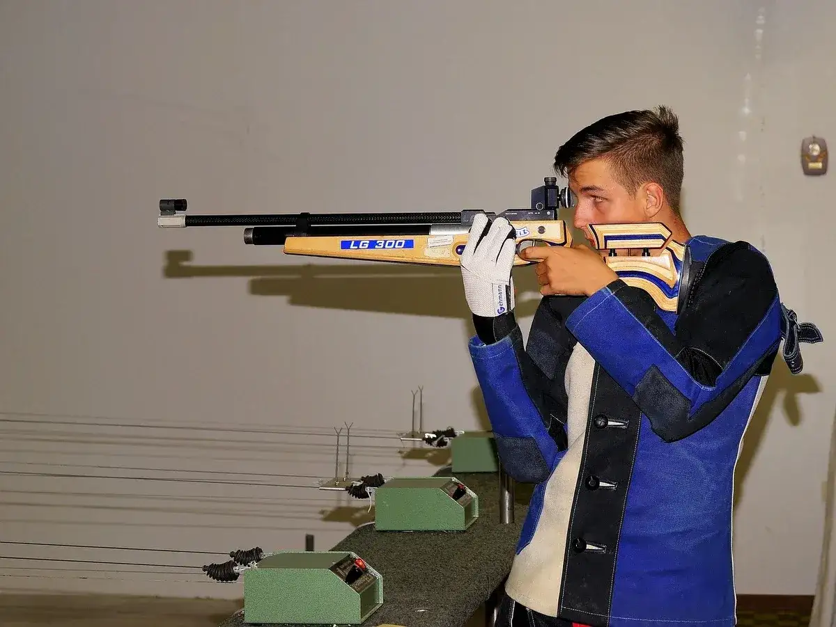 Młody strzelec z białymi rękawiczkami celuje z karabinu sportowego. Posiadanie pozwolenia na broń to pierwszy krok do tej dyscypliny.