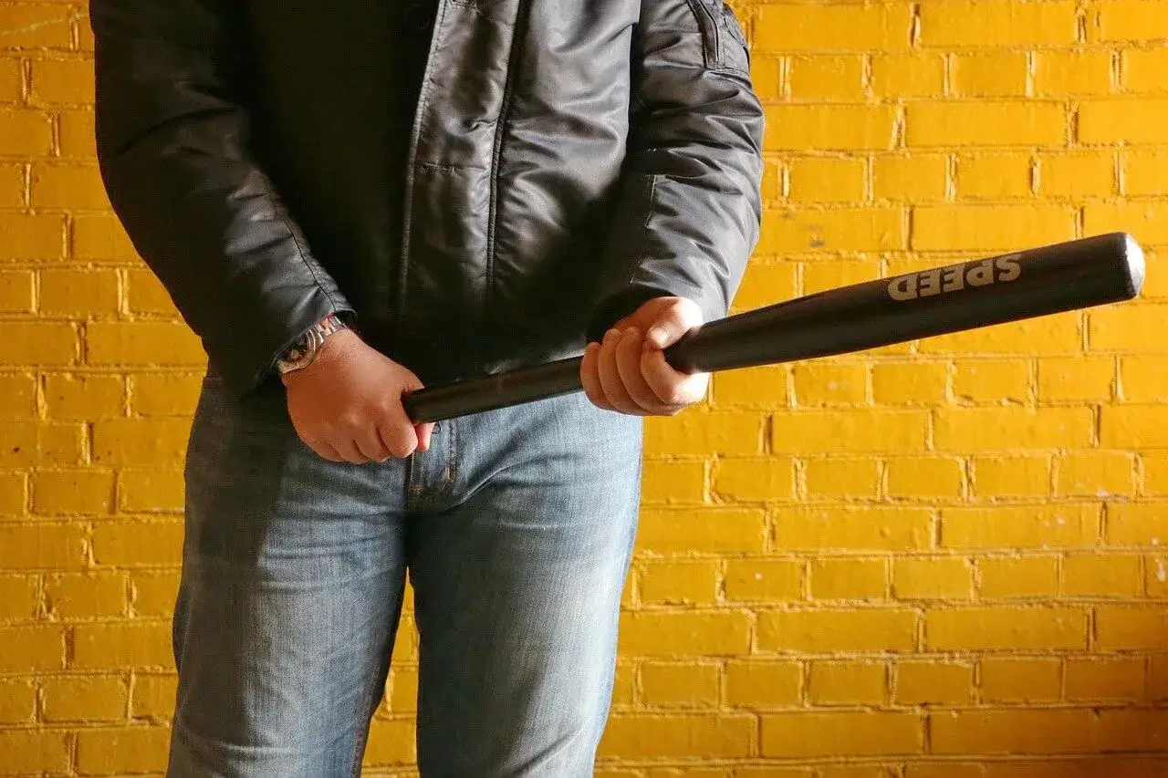 Mężczyzna w kurtce i jeansach trzyma kij baseballowy, gotowy do rozboju.