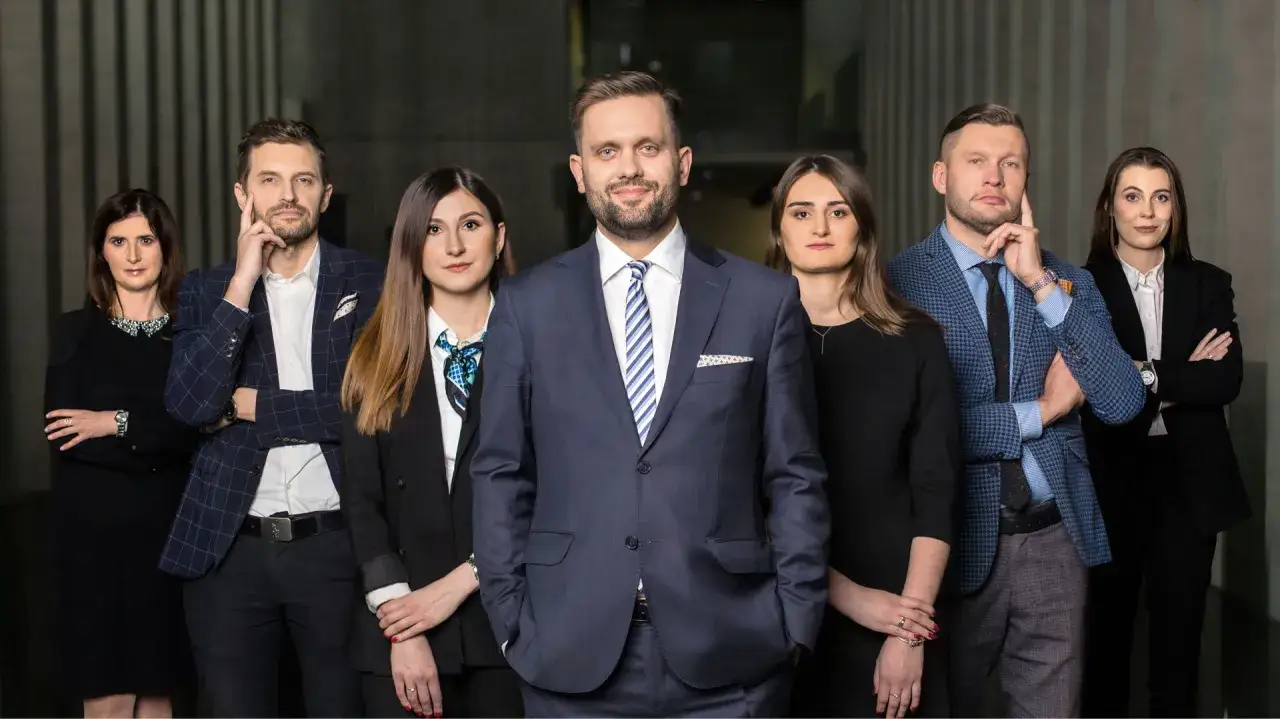 Grupa prawników w garniturach i strojach biznesowych, stojąca przed nowoczesną architekturą.