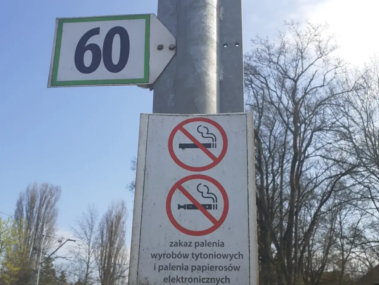 Znak zakazu palenia wyrobów tytoniowych i papierosów elektronicznych. Obok znak ograniczenia prędkości do 60.