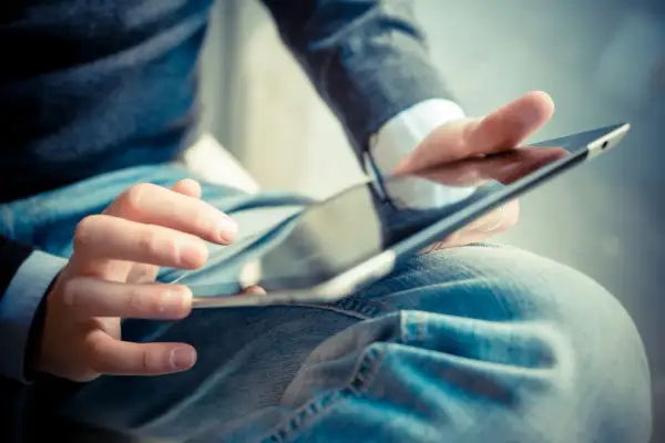 Dłonie mężczyzny w dżinsach i swetrze korzystają z tabletu. Może szuka ulgi na internet co ile lat?