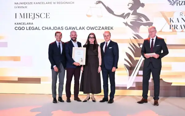 Cztery osoby w garniturach stoją na scenie, odbierając nagrodę.