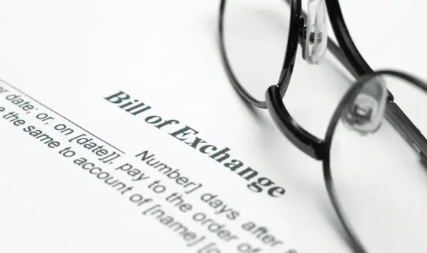 Okulary leżą na dokumencie "Bill of Exchange", czyli wekslu. Widoczne są fragmenty tekstu dotyczące daty i płatności.
