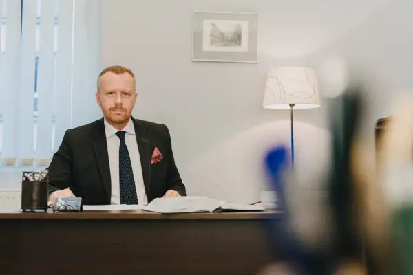 Mężczyzna w garniturze siedzi przy biurku, przed nim otwarta księga.