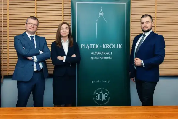 Trzy osoby w garniturach stoją przed zielonym banerem kancelarii.