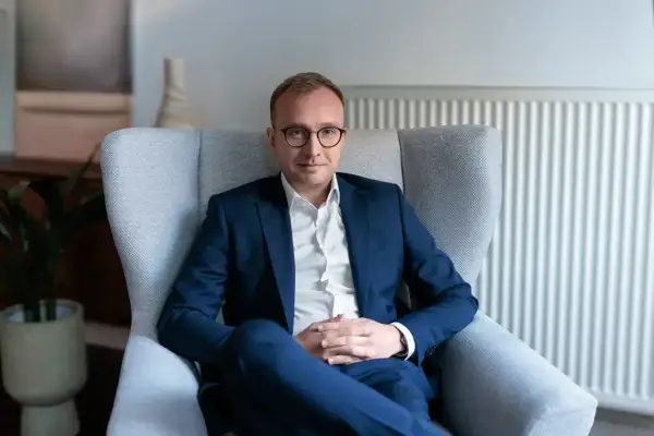 Mężczyzna w garniturze siedzi w fotelu, w tle kaloryfer i roślina.