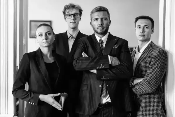 Cztery osoby w garniturach, w tym dwie kobiety i dwóch mężczyzn, stoją w rzędzie.