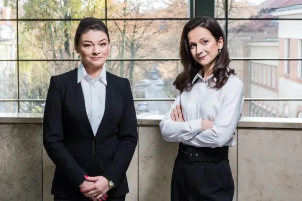 Dwie kobiety w strojach biznesowych stoją przed oknem z widokiem na miasto.