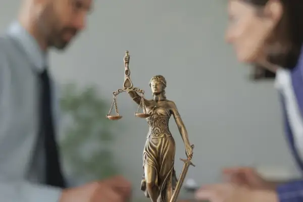 Figurka Temidy z wagą i mieczem na tle niewyraźnych postaci prawników.