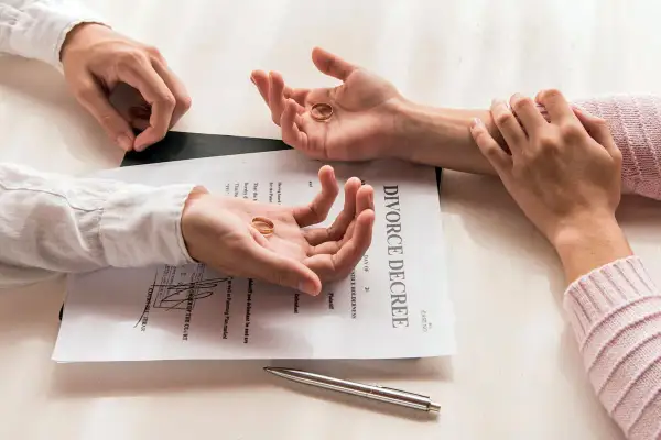 Dwie dłonie trzymają obrączki, leżące na dokumencie "DIVORCE DECREE". Symboliczny koniec małżeństwa, czas na rozwód.