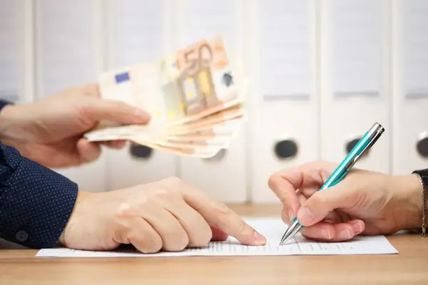 Dwie osoby przy biurku. Jedna podaje plik banknotów 50 euro, druga podpisuje dokument. To może być moment, kiedy należy się odprawa.