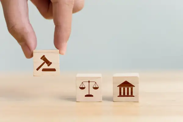 Dłoń układa kostki z symbolami prawa: młotek sędziowski, waga sprawiedliwości i budynek sądu, symbolizujące jurysdykcję.