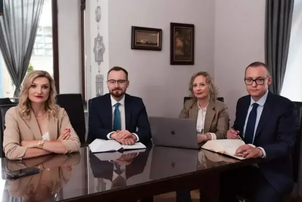 Cztery osoby w strojach biznesowych siedzą przy stole w sali konferencyjnej.