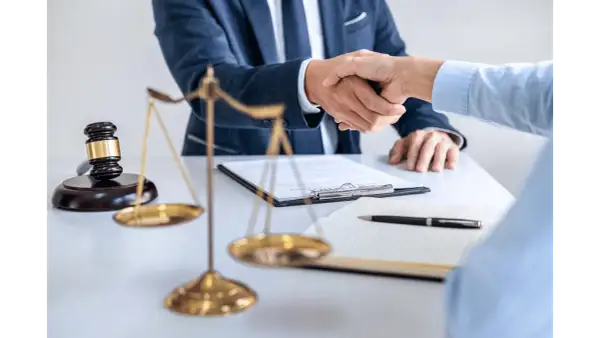 Dwóch prawników ściska sobie dłonie przy biurku, na którym leży młotek sędziowski i waga sprawiedliwości. Sprawa 157 kk zakończona sukcesem.