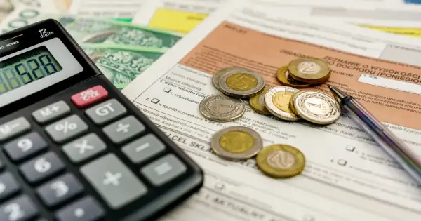 Kalkulator, monety i dokumenty podatkowe leżą na stole, czekając na rozliczenie. Kiedy zwrot podatku jest blisko, liczenie staje się prostsze.