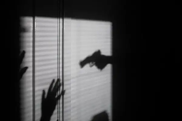 Cień dłoni z pistoletem grozi dwóm dłoniom, które próbują się zasłonić. To scena jak z filmu o świadku koronnym.