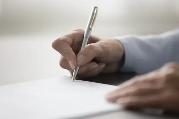 Dłoń pisze długopisem na papierze, przygotowując dokument. Dowiedz się, jak napisać testament.